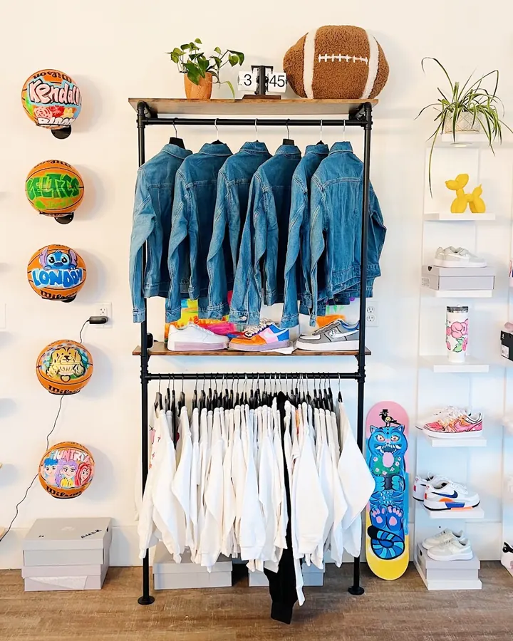 A rail of hand painted denim jackets and white tees in the studio, with painted basketballs and skateboards on the wall behind