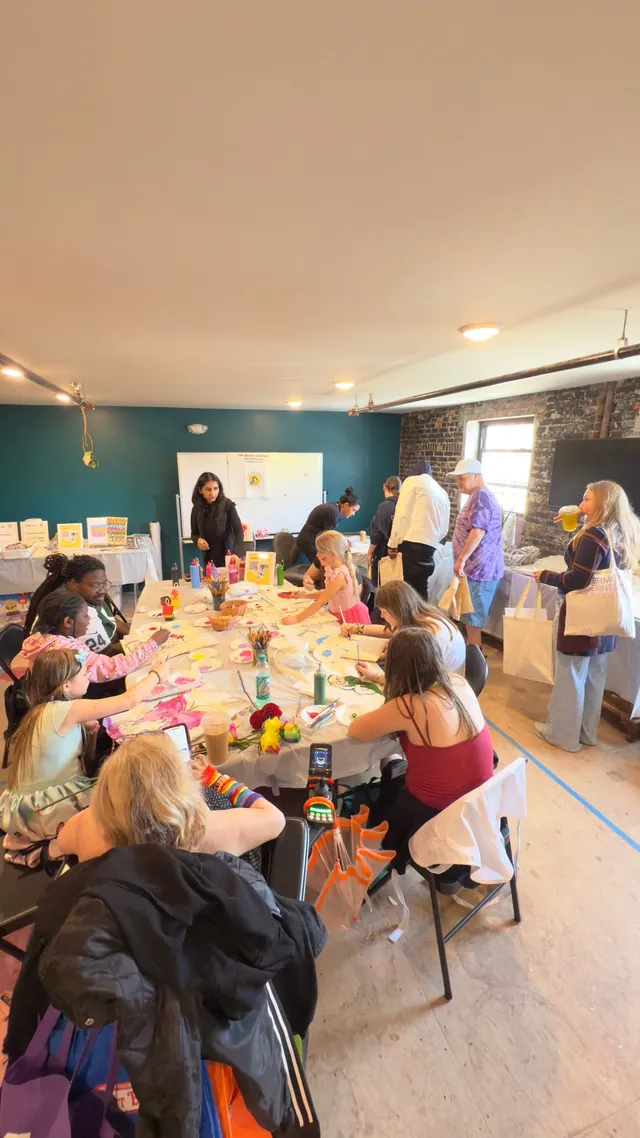 About ten kids craft along a long table in a room with a teal wall while an instructor leads from the whiteboard