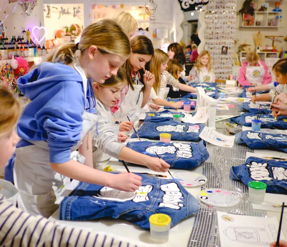 Girls paint denim jackets along a long party table with a sequin runner
