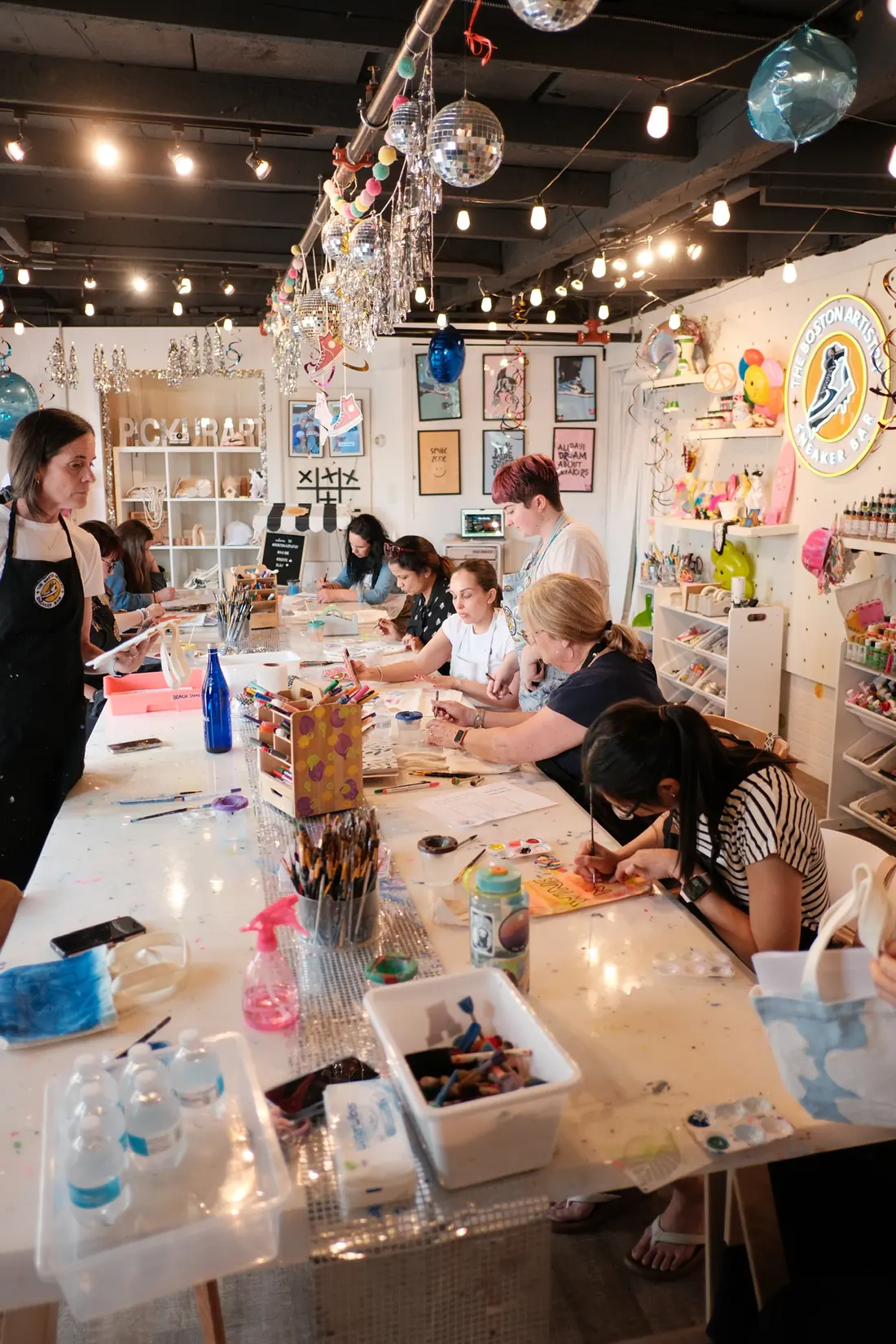 Adults painting together at a long table during a workshop at The Boston Artistry