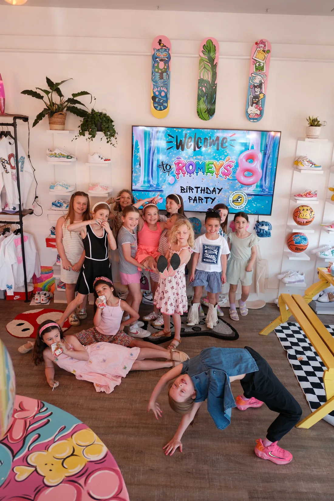 About thirteen girls pose before a birthday welcome screen in the studio while one does a backbend on the floor