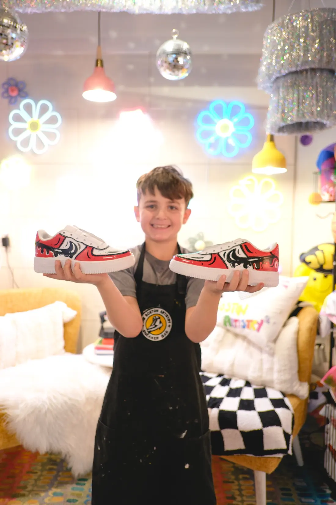 A smiling boy holds up a finished pair of custom painted sneakers