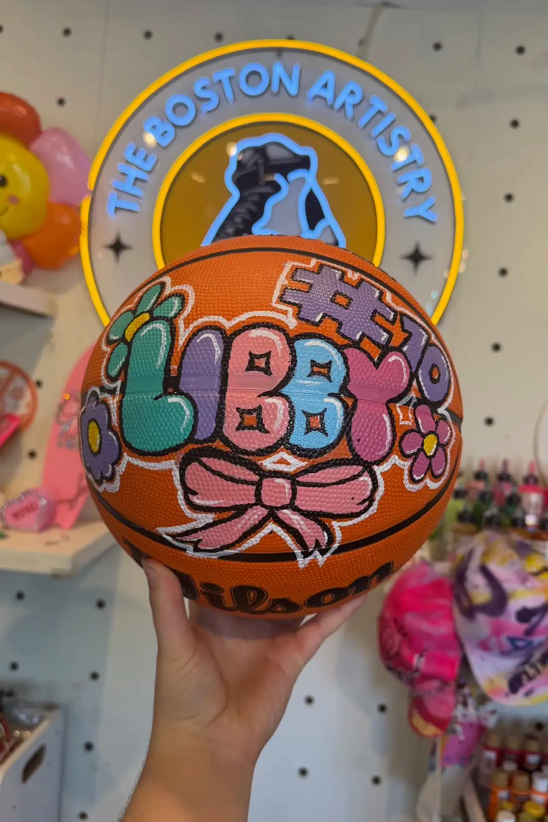 A finished basketball painted with a name in bubble letters and a pink bow