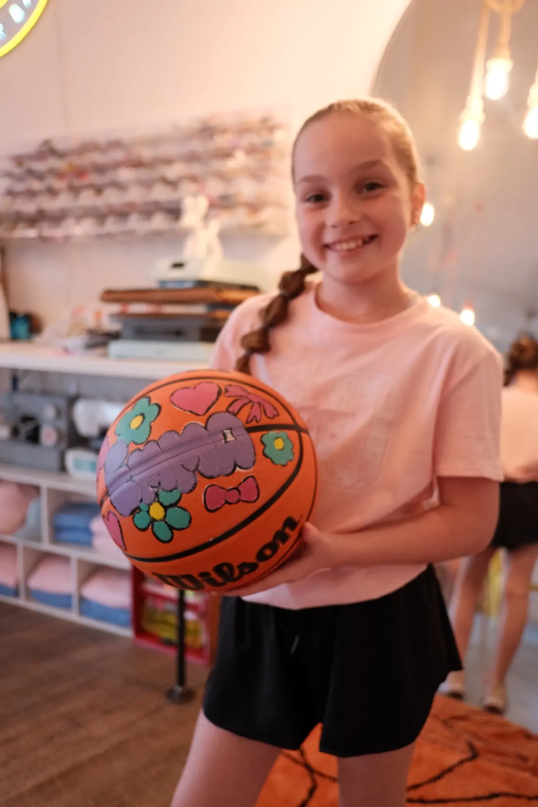 A girl holds up a basketball she painted with flowers