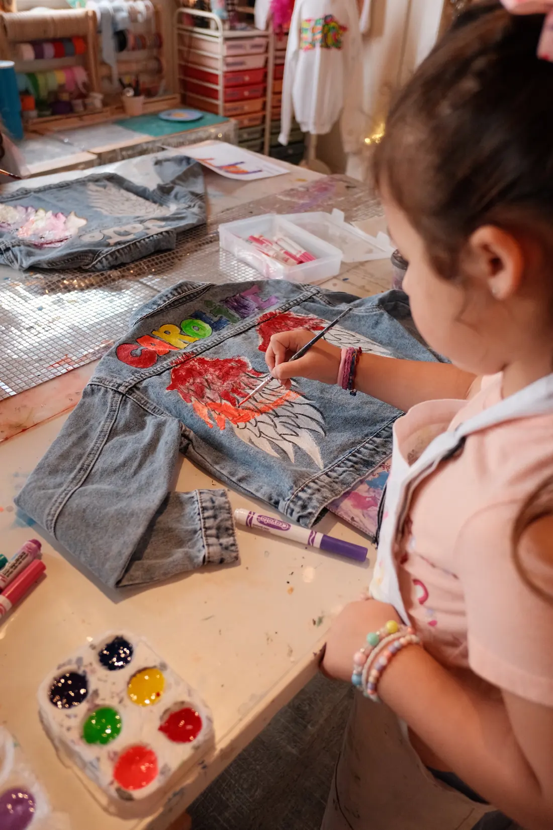 A girl paints the back of a denim jacket at a party in the studio