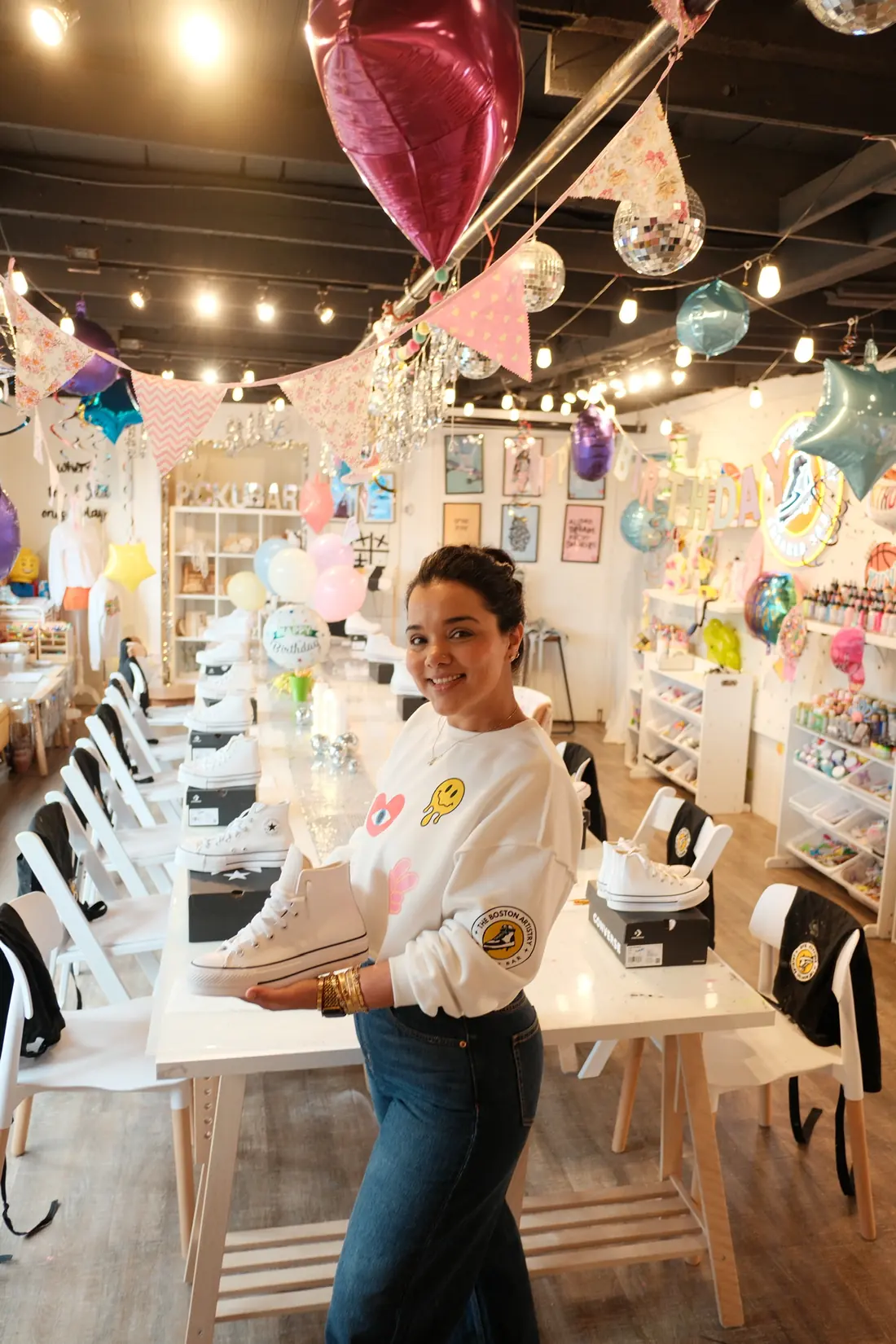 Nandita, founder of The Boston Artistry, smiling with a blank white high top sneaker beside a party table in the Hingham studio
