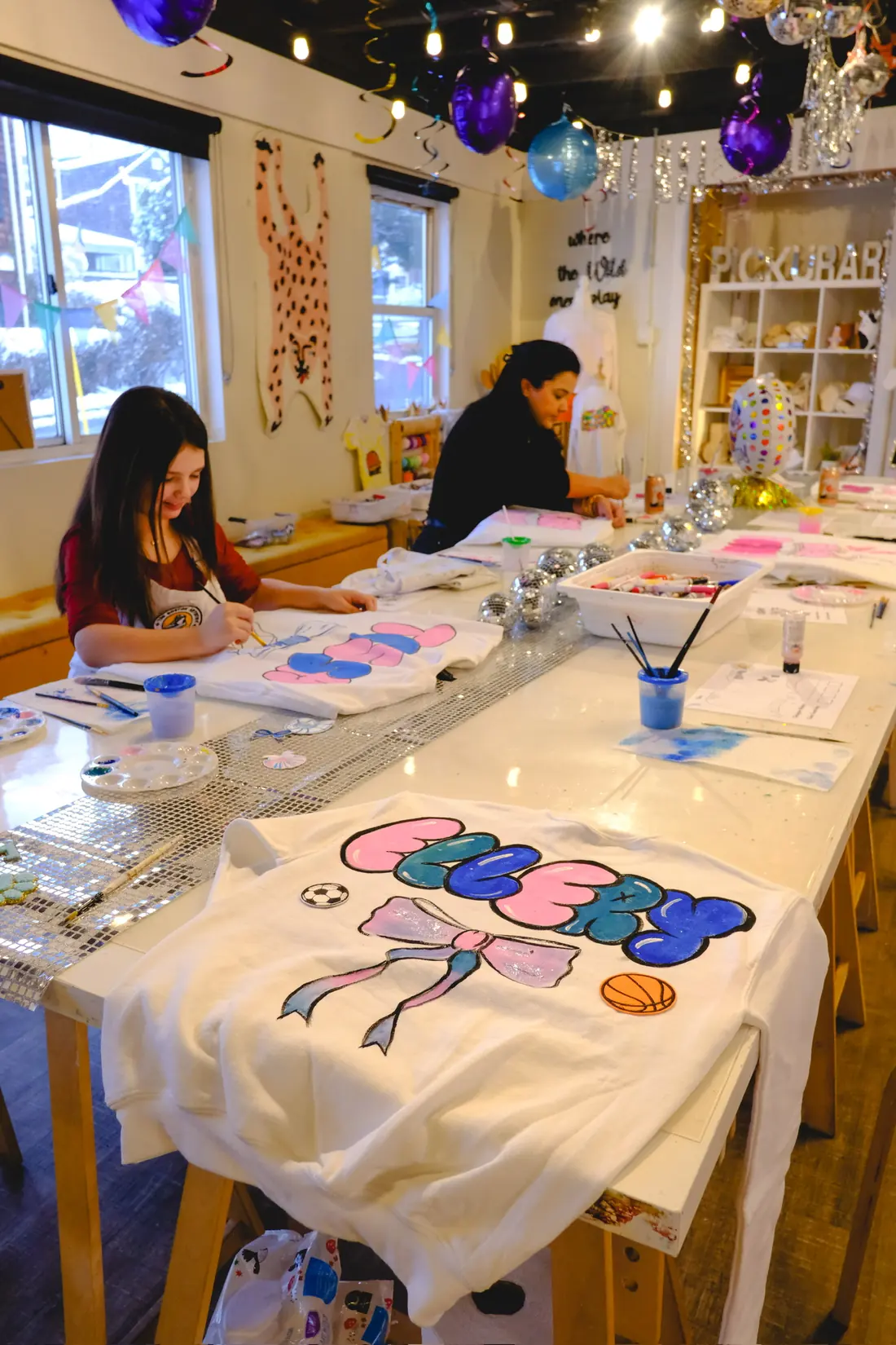 A white sweatshirt painted with a name and sports balls on the party table